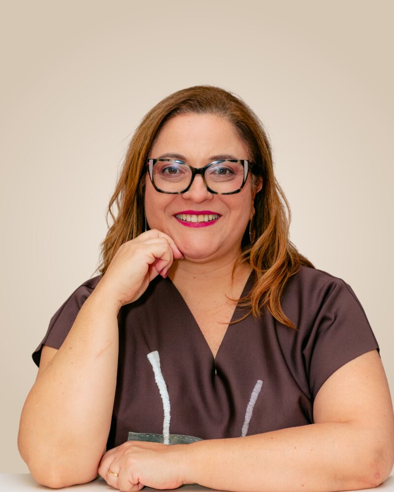 Renata Bertran, psicóloga, de óculos, sorrindo com a mão no rosto